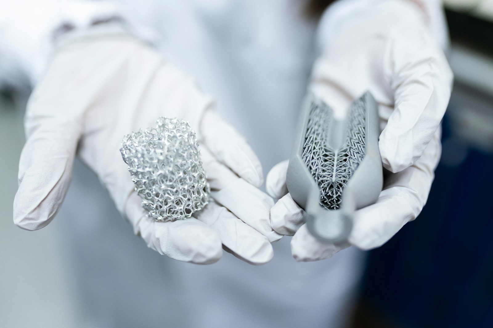 White-gloved hands holding two porous metal specimens